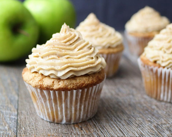 Spiced apple cake or cupcakes made with Raven's Nest mulling spice topped with creamy frosting, garnished with cinnamon surrounded by fresh granny smith apples
