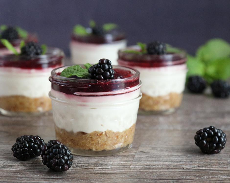 Individual cheesecake cups in mason jars topped with blackberry jam and fresh blackberries