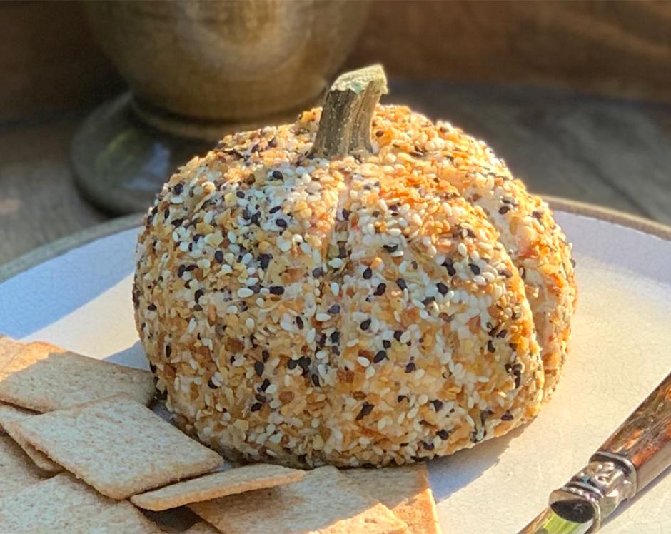 Pumpkin shaped cheese ball made with Raven's Nest garden party mix and coated with everything but the bagel seasoning and served with crackers