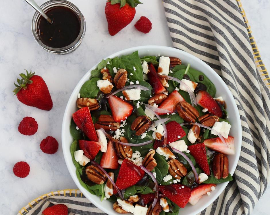 Homemade raspberry vinaigrette salad dressing recipe made with Raven's Nest raspberry jalapeno jam tossed with a spinach salad with fresh strawberries, feta cheese, pecans, and slivered onions