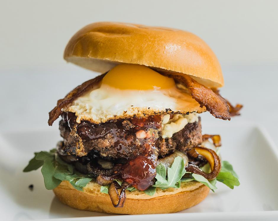 Gourmet grilled Red White and Bleu burger topped with caramelized onions, arugula, fried egg, bleu cheese crumbles, bacon, and Raven's Nest jam